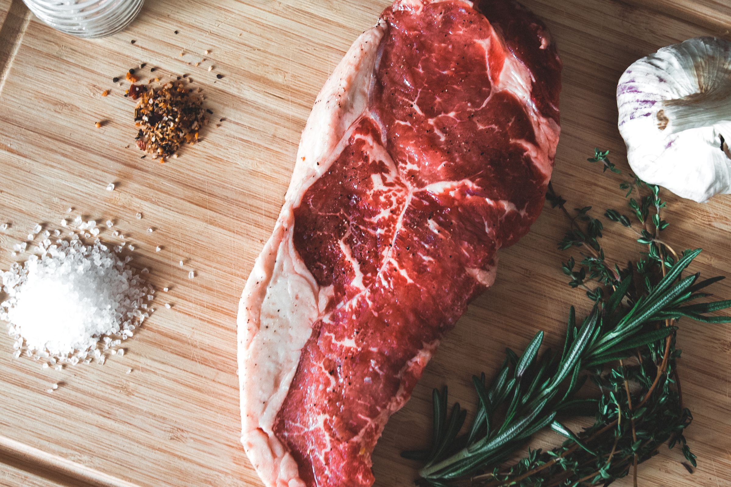 Rauwe entrecote met grof zeezout, knoflook en rozemarijn op een houten plank